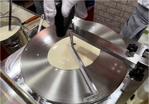 回転式クレープスプレッダー（トンボ）のハンドルを回して生地を延ばし始める工程